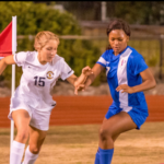 Two girls playing soccer on a field.