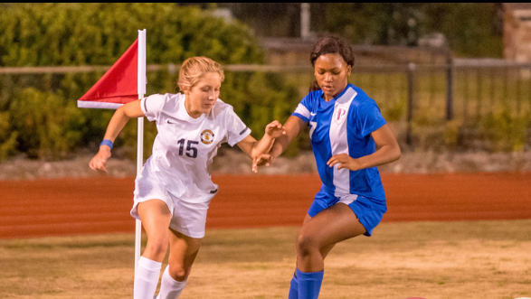 Two girls playing soccer on a field.